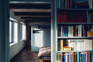 Blick in ein Schlafzimmer mit einem Bücherregal vor der Tür