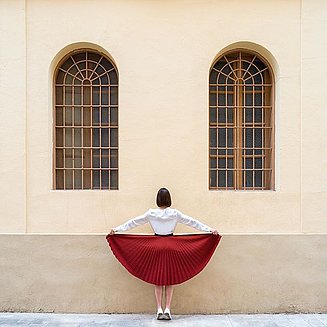 Frau mit rotem Rock vor einem Haus