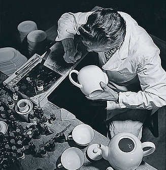 Porzellanarbeiter bei der Arbeit, zieht Dekorlinien an einer Tee-Kanne 